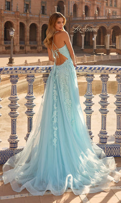 Wearing the La Femme 33715 long prom dress in light blue tulle with lace embroidery, a woman stands by a decorative railing in an outdoor plaza.