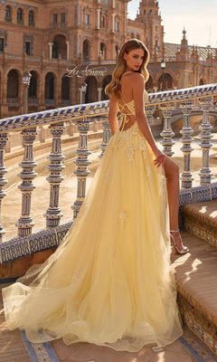 A woman in the La Femme 33716 long prom dress, featuring yellow lace embroidery and a train, stands on an ornate stone balcony overlooking a historic building in daylight.