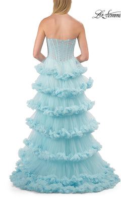 A woman stands with her back to the viewer, showcasing the Strapless Tiered Prom Ball Gown: La Femme 33717—a stunning strapless sweetheart dress made from layers of light blue tulle with dramatic, ruffled tiers. Set against a white background, the La Femme logo is displayed in the upper right corner, emphasizing this elegant and voluminous ball gown.