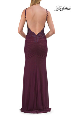A woman stands facing away, wearing the La Femme 33721 Open-Back Sheer-Corset Prom Gown: a backless, floor-length burgundy evening dress with thin straps and lace detailing at the top.