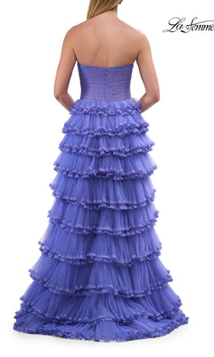 Wearing the La Femme 33727 long prom dress, a woman stands with her back to the camera, showcasing the strapless, tiered tulle ball gown with a corset bodice and layers of ruffled purple fabric cascading elegantly to the floor.