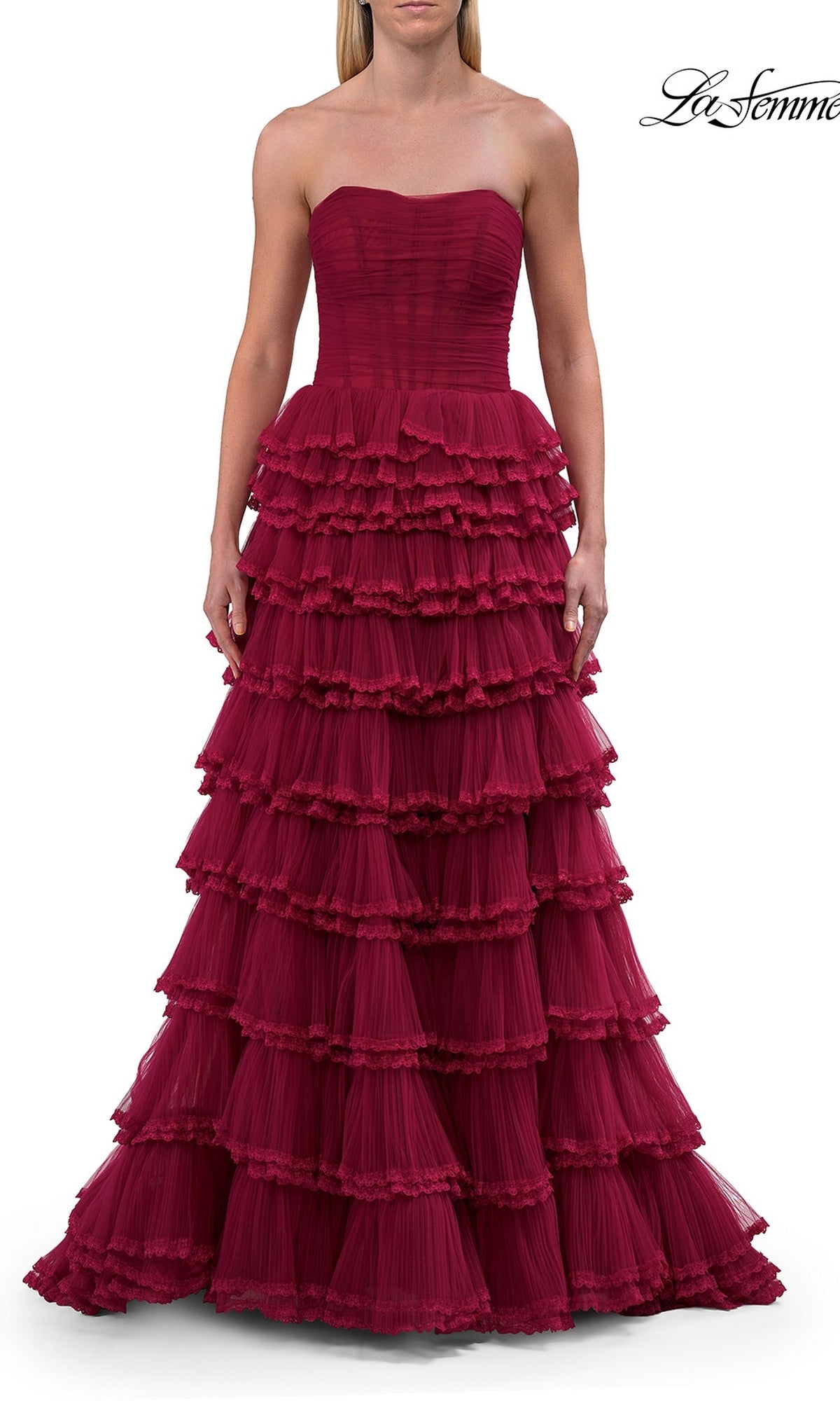A woman stands against a white background wearing the Long Prom Dress: La Femme 33727—a strapless, floor-length dark red gown featuring multiple tiered ruffles and a fitted corset bodice.