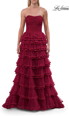 A woman stands against a white background wearing the Long Prom Dress: La Femme 33727—a strapless, floor-length dark red gown featuring multiple tiered ruffles and a fitted corset bodice.