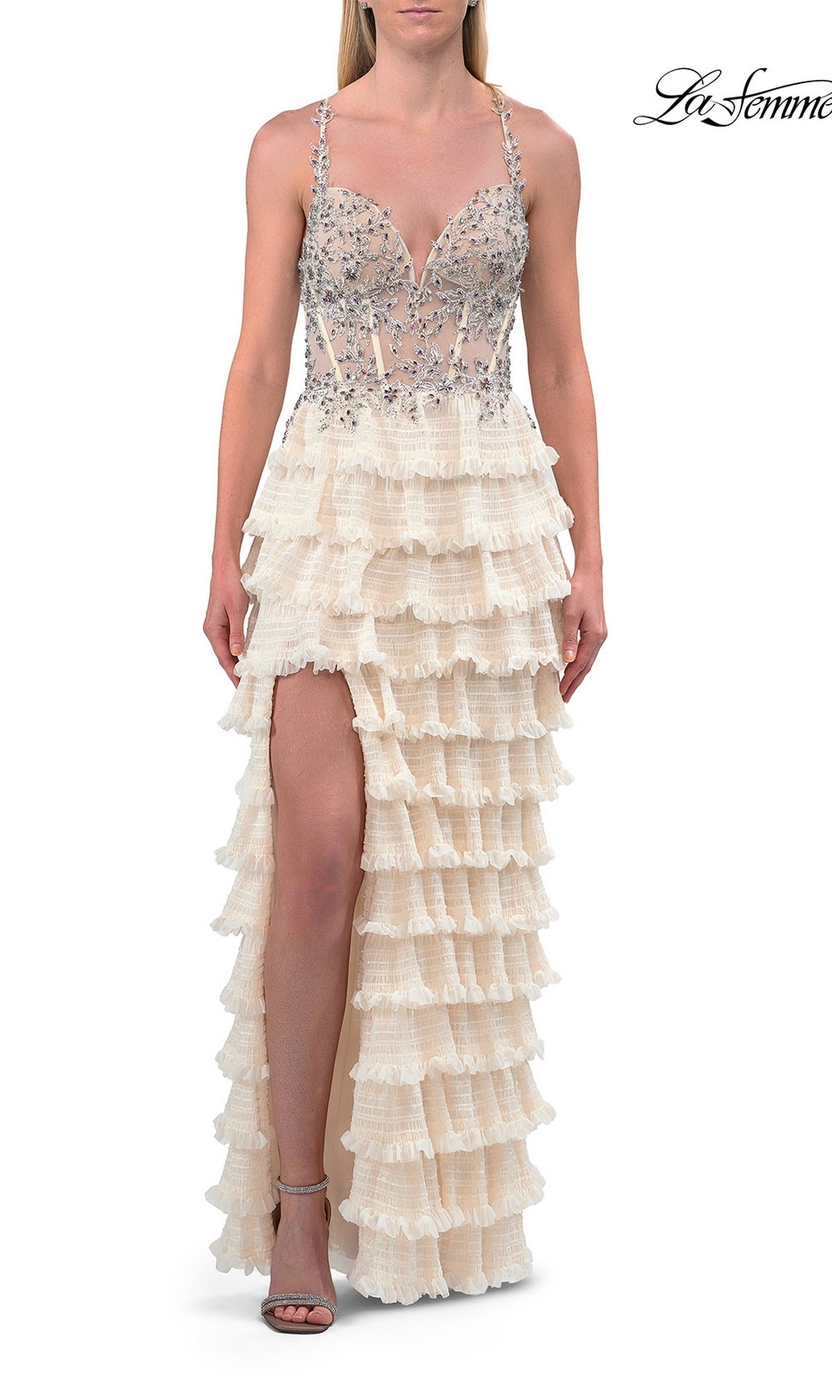 A woman wearing the La Femme 33751 Beaded-Corset Ruffle Prom Gown in Champagne—featuring a beaded sheer corset bodice, tiered ruffle skirt, and high front slit—paired with strappy heels, is photographed against a white background.