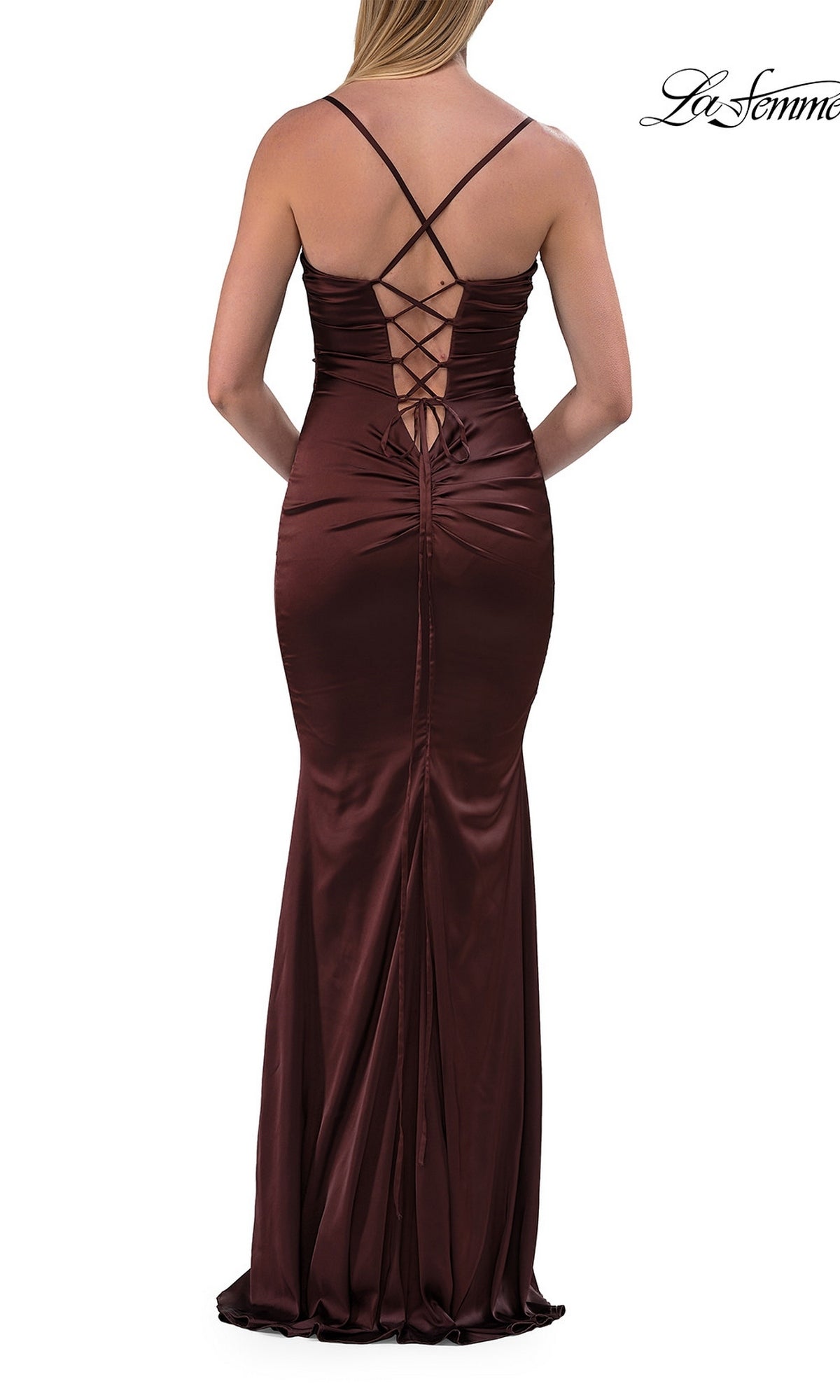 A woman stands with her back to the camera wearing the La Femme 33764 Criss-Cross Open-Back Prom Gown—a long, fitted satin dress in dark brown with thin straps and crisscross lace-up detailing at the back.