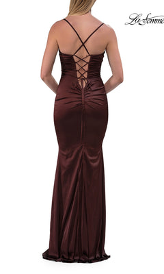 A woman stands with her back to the camera wearing the La Femme 33764 Criss-Cross Open-Back Prom Gown—a long, fitted satin dress in dark brown with thin straps and crisscross lace-up detailing at the back.