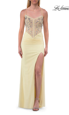 A woman wearing the Sheer-Corset Long Prom Dress: La Femme 33783 in pale yellow—a sleeveless gown with an embellished bodice, sheer paneling, thigh-high slit, open back, and delicate floral embroidery for a touch of romance—paired with strappy sandals.