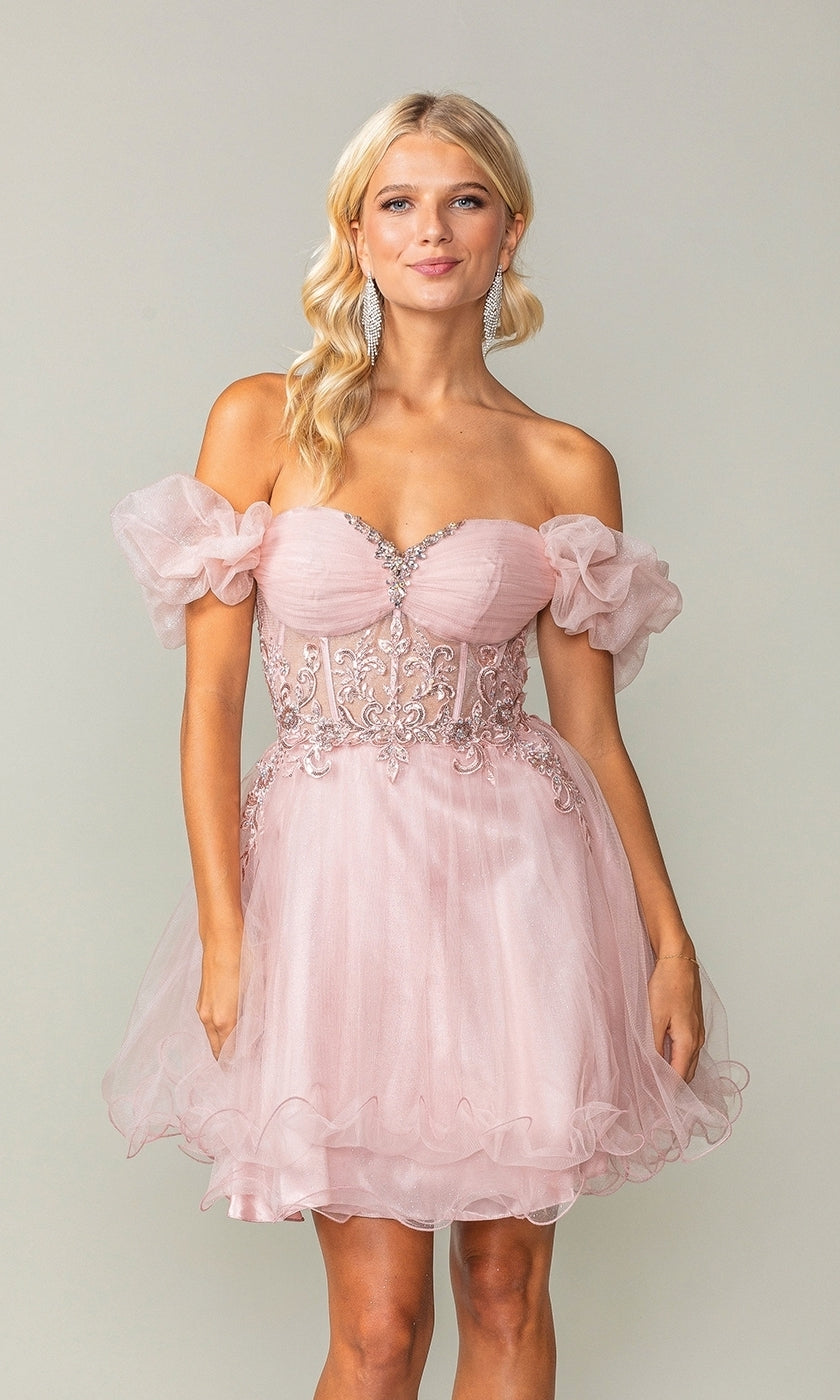 A woman wears the Ruffle-Sleeve Short Corset Homecoming Dress 3379, featuring off-the-shoulder light pink tulle, puffed sleeves, and silver embroidery on the corset bodice, standing against a plain background.