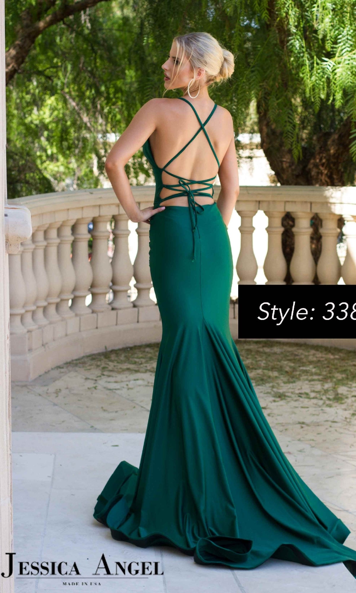 Woman in a floor-length emerald green Jessica Angel 338 strappy long mermaid prom dress with crisscross back, standing on a terrace. Text: 