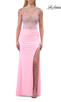 A woman wearing a baby pink, floor-length Lace-Up Sheer-Corset Prom Gown (La Femme 33808) featuring a fitted, beaded bodice with beaded-lace appliques, thin straps, and a high slit on the left skirt.