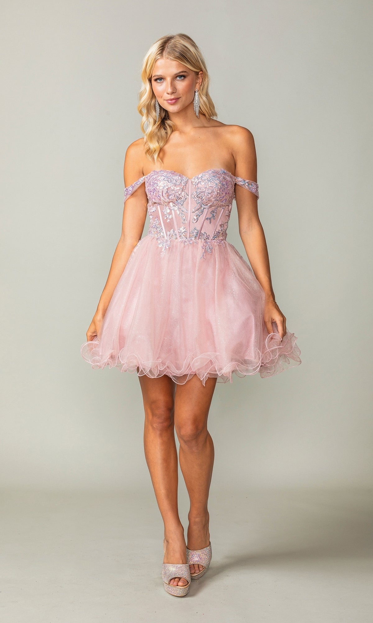 A woman wears the Dancing Queen 3383 short corset homecoming dress featuring silver glitter embellishments, a fitted sheer bodice, and a tulle skirt, paired with light-colored heels.