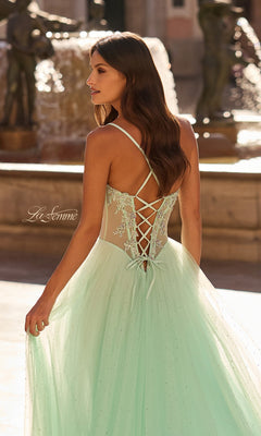 A woman stands outdoors near a fountain wearing the La Femme 33860 long prom dress, which features a light green embroidered corset bodice and a flowing tulle skirt.