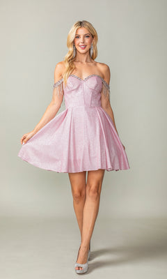 A woman models the Fringed Off-Shoulder Short Homecoming Dress 3392 in light pink with sparkly silver fringe and a corset bodice, paired with silver heels, against a plain background.