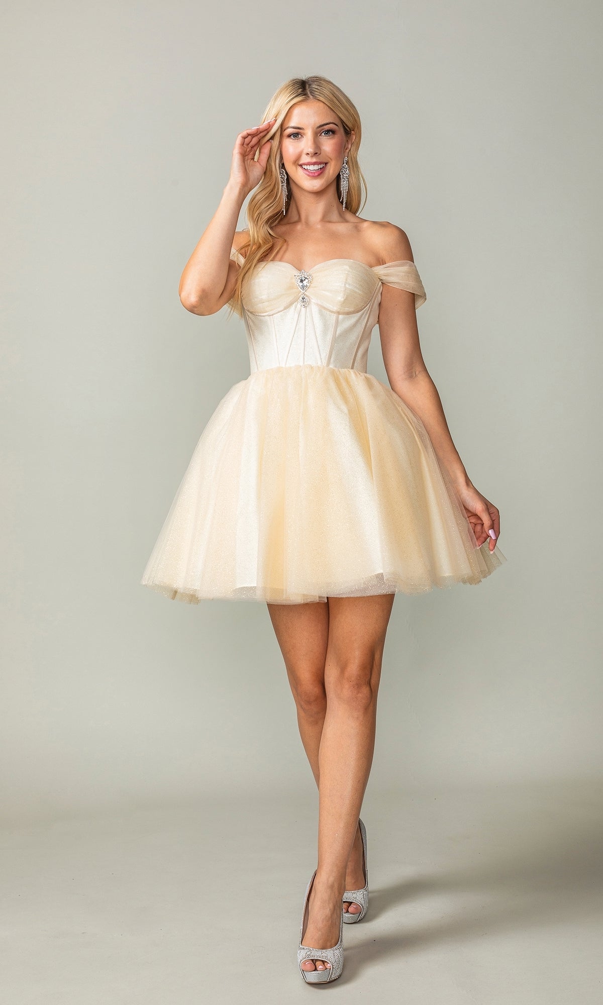 A woman poses in the Off-Shoulder Short Fit-and-Flare Hoco Dress 3394, featuring a corset-style bodice and light beige tulle, styled with silver high heels against a plain background.