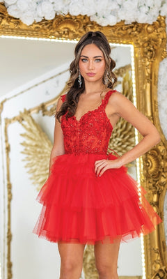 A woman stands before a gold-framed mirror wearing the Short Babydoll Prom Dress: Dancing Queen 3402, featuring floral embellishments and a sheer corset bodice. White flowers adorn the top of the mirror.