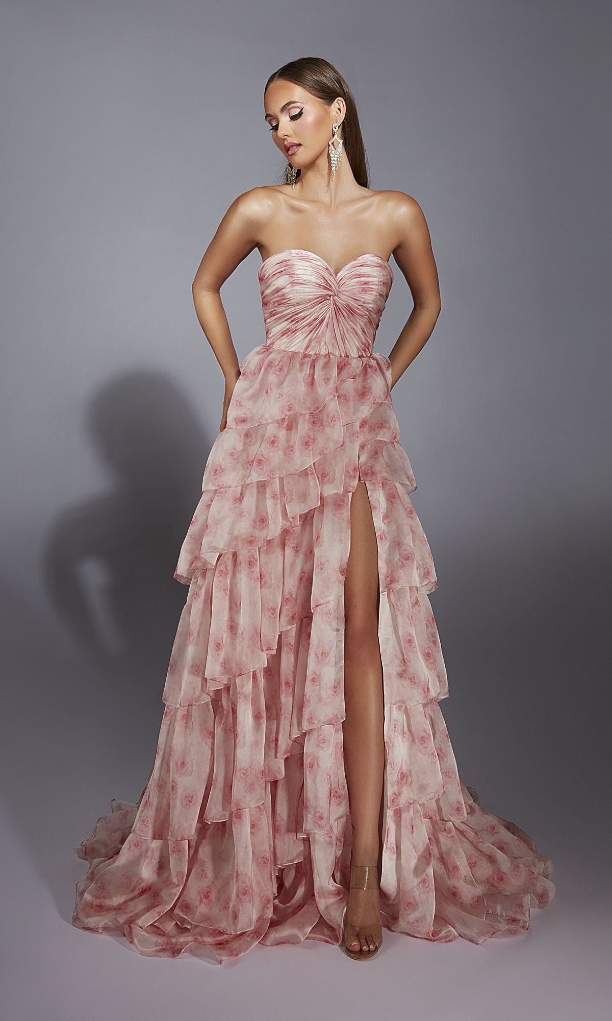 Model wears the Pink Floral Prom Ball Gown: Aerie Couture 340, featuring a strapless sweetheart ruched bodice, tiered pink layers, floral pattern, and thigh-high slit, posed against a plain gray background.