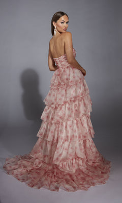 A woman stands against a gray background, wearing the Pink Floral Prom Ball Gown: Aerie Couture 340 with a strapless sweetheart ruched bodice, tiered pink floral layers, and a long train as she looks over her shoulder.