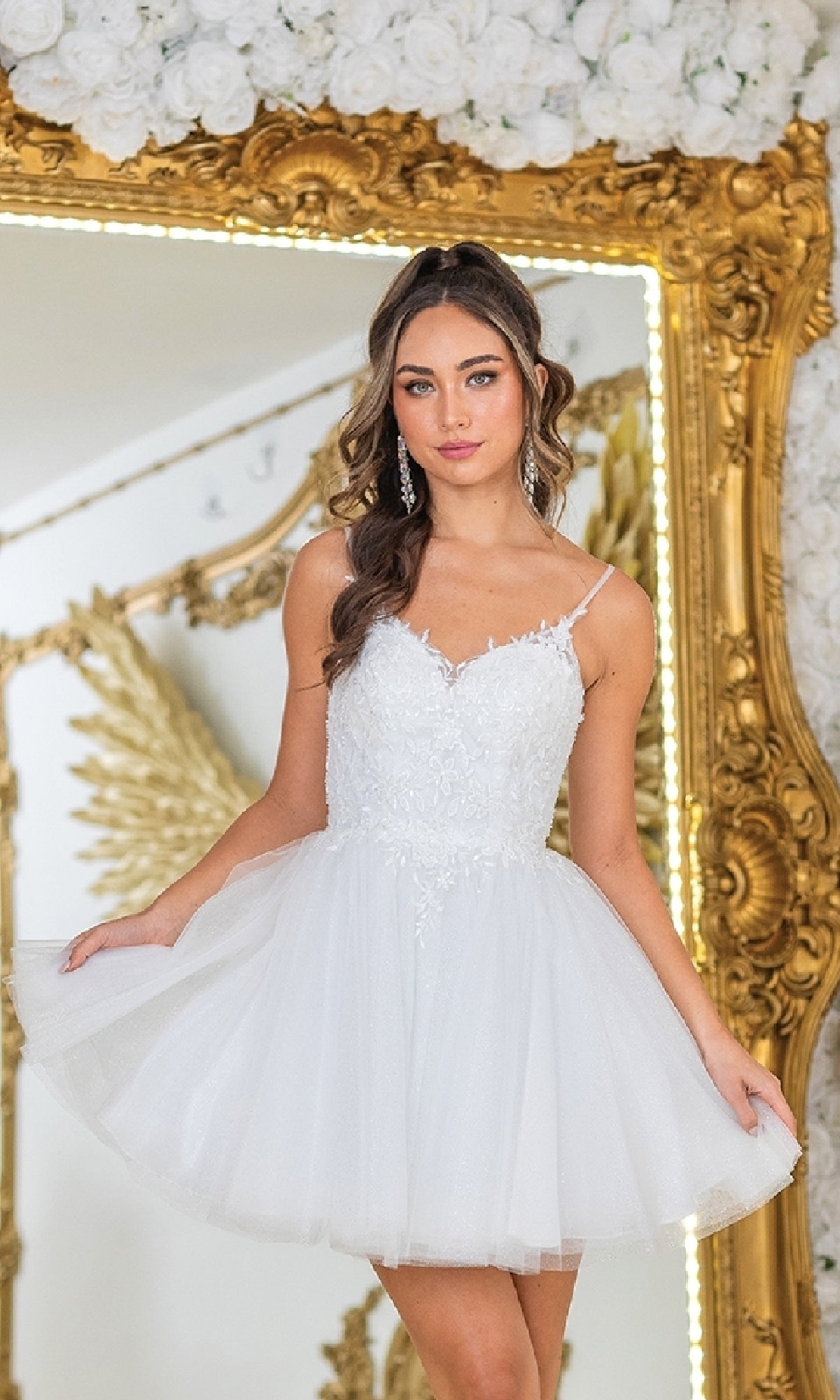 A woman wearing the Short Glitter-Tulle Prom Dress: Dancing Queen 3413, featuring a lace-up corset and sparkling tulle, stands in front of an ornate gold mirror and floral decor.
