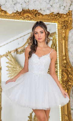 A woman wearing the Short Glitter-Tulle Prom Dress: Dancing Queen 3413, featuring a lace-up corset and sparkling tulle, stands in front of an ornate gold mirror and floral decor.