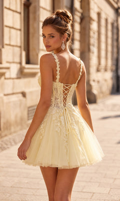 Wearing the La Femme 34146 short homecoming dress, a woman stands on a city street looking over her shoulder. The light yellow lace dress features elegant embroidery, floral details, and a corset back with a flattering fit-and-flare silhouette—making it the perfect choice for a cute homecoming look.