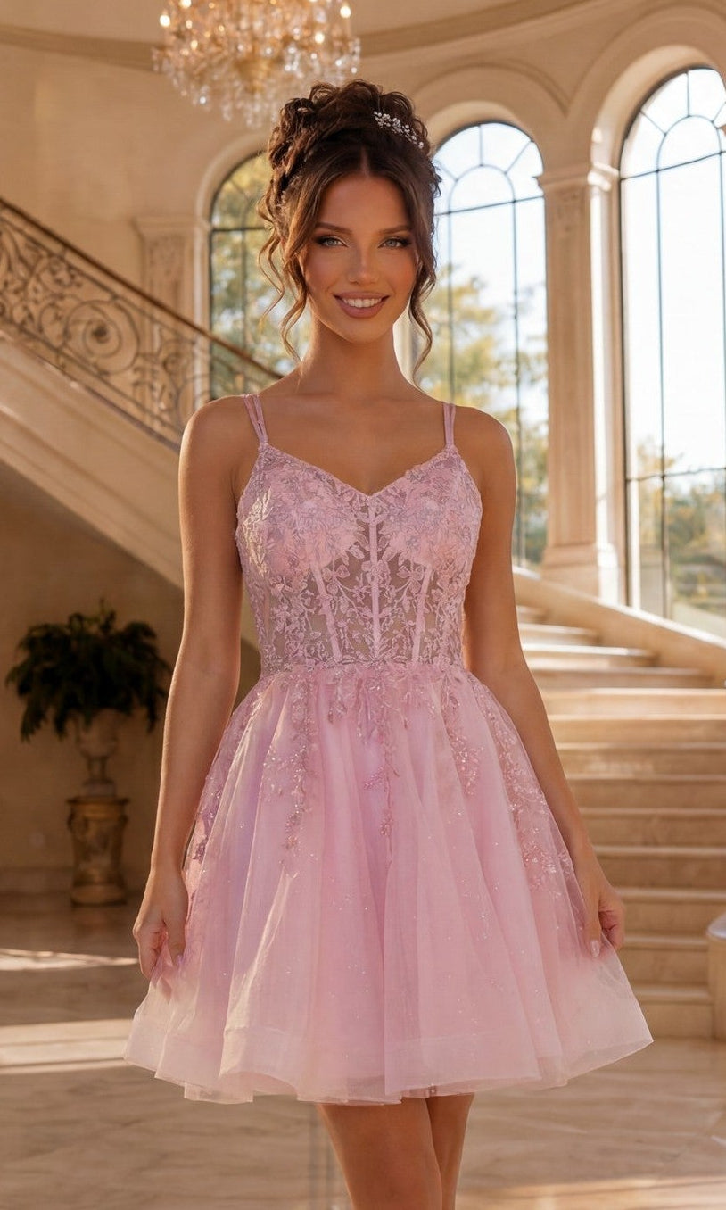 A woman stands indoors on a staircase, smiling at the camera and wearing the Short Corset Prom Dress: Dancing Queen 3415 in pink. Her hair is styled and the dress features lace and tulle details.
