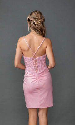 A woman in the Dancing Queen 3427 Short Prom Dress, pink and sleeveless with a lace-up back and fitted silhouette, stands facing away from the camera against a plain gray background.