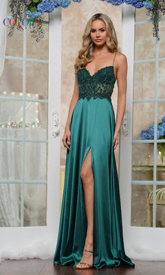 A woman poses indoors in the Sheer-Corset Long Prom Dress: Colors Dress 3436, featuring teal satin, a beaded corset bodice, spaghetti straps, and a thigh-high slit. She has long wavy hair and stands in front of glass doors.