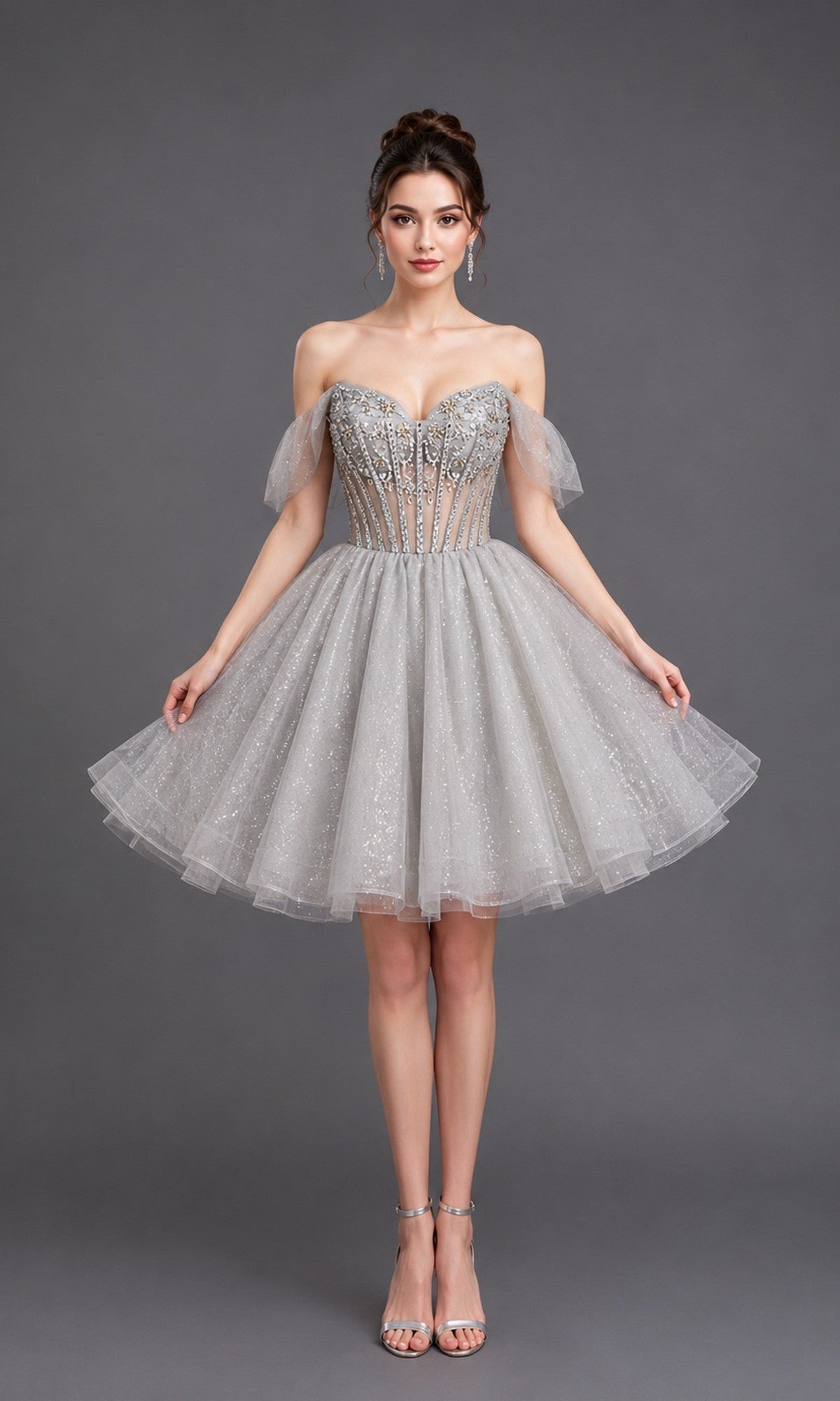 Wearing the Short Homecoming Dress: Dancing Queen 3438 in silver, a woman poses against a plain gray background. The strapless design features a fitted bodice and sparkly tulle skirt, accentuating her figure as shimmering details catch the light.