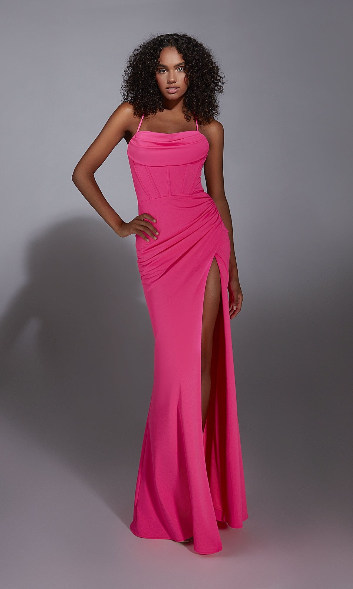 A woman models the Aerie Couture 343 Long Prom Dress, a bright pink floor-length gown featuring a corset bodice and thigh-high slit, against a plain gray background.