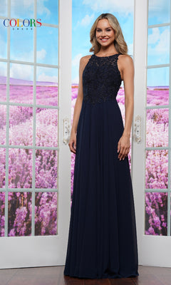 A woman stands indoors before glass doors, wearing the High-Neck Long Prom Dress: Colors Dress 3440 in navy blue with lace bodice; a field of purple flowers is visible outside.