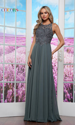 A woman stands indoors in front of large windows overlooking a field of purple flowers, wearing the High-Neck Long Prom Dress: Colors Dress 3440—a floor-length, sleeveless grey gown with lace bodice detailing.
