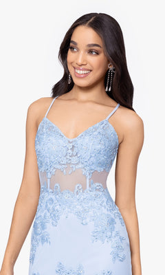 A woman smiles and looks to the side wearing the Blondie Nites Long Mermaid Prom Dress 3448BN, featuring light blue fabric, spaghetti straps, embroidered lace appliques, and sheer detailing.