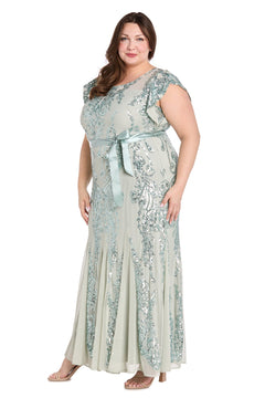 A woman stands against a white background, wearing the Plus-Size Sage Green Formal Dress: R&M Richards 3465W, a floor-length gown with silver sequin accents and a satin ribbon belt.