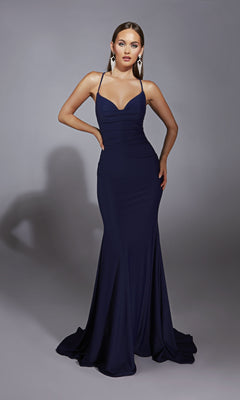 A woman poses in the Aerie Couture 346 Cowl-Neck Long Prom Dress, a fitted navy blue gown with spaghetti straps and an open back, styled with statement earrings against a gray background. This formal dress exudes sophistication.