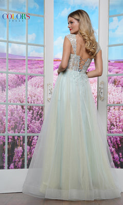A woman in the Colors Dress 3498 Off-Shoulder Glitter Tulle Prom Ball Gown stands with her back to the camera, framed by glass doors and a purple flower field beyond.