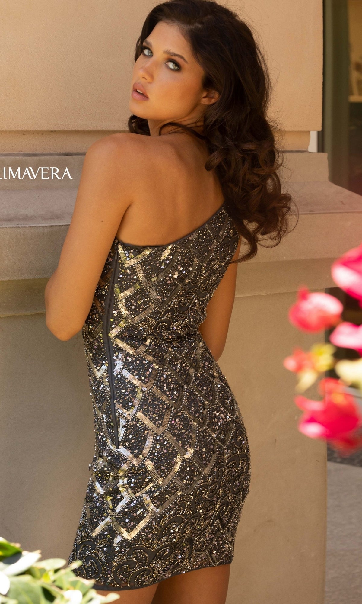 A woman with long brown hair stands outdoors, wearing the One-Shoulder Short Sequin Beaded Party Dress 3504D and looking over her shoulder toward the camera.