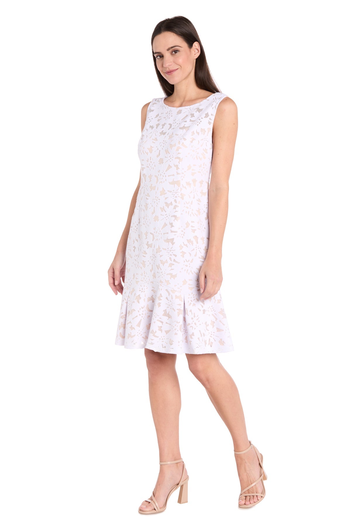 A woman wears the R&M Richards 3506P Petite White Lace Party Dress with a floral pattern and flared hem, paired with nude heeled sandals, standing against a white background.