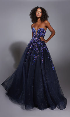 A woman wears the Navy Blue Prom Ball Gown: Aerie Couture 350, featuring a strapless fitted bodice and an A-line glitter tulle skirt with purple floral embellishments, standing against a plain background.