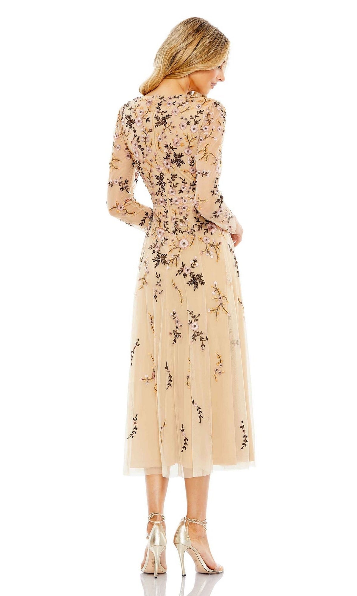A woman faces away, wearing the Mac Duggal Midi Floral Wedding Guest Dress—beige with long sleeves and floral embroidery—paired with metallic heels against a white background.