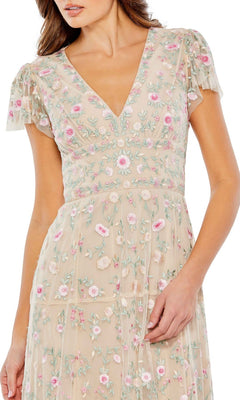 Woman models the Mac Duggal 35104 Embroidered Wedding-Guest Dress, featuring a beige color, pink floral embroidery, and short ruffled sleeves, standing with one hand resting at her side.