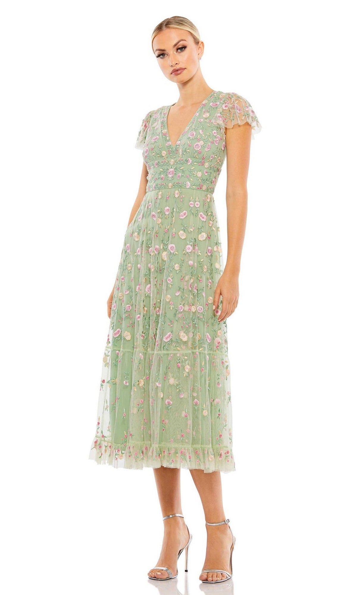 A woman wears the Mac Duggal 35104 embroidered wedding-guest dress in light green with short sleeves and silver high-heeled sandals, standing against a white background.