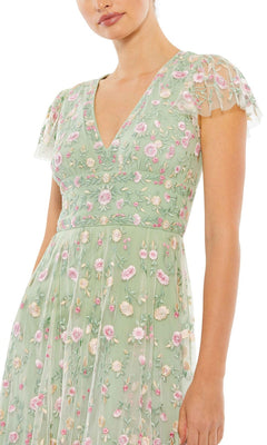 A person wears the Mac Duggal 35104 embroidered wedding-guest dress in light green with short sheer sleeves and pink floral accents, shown from mid-face to below the waist against a white background.