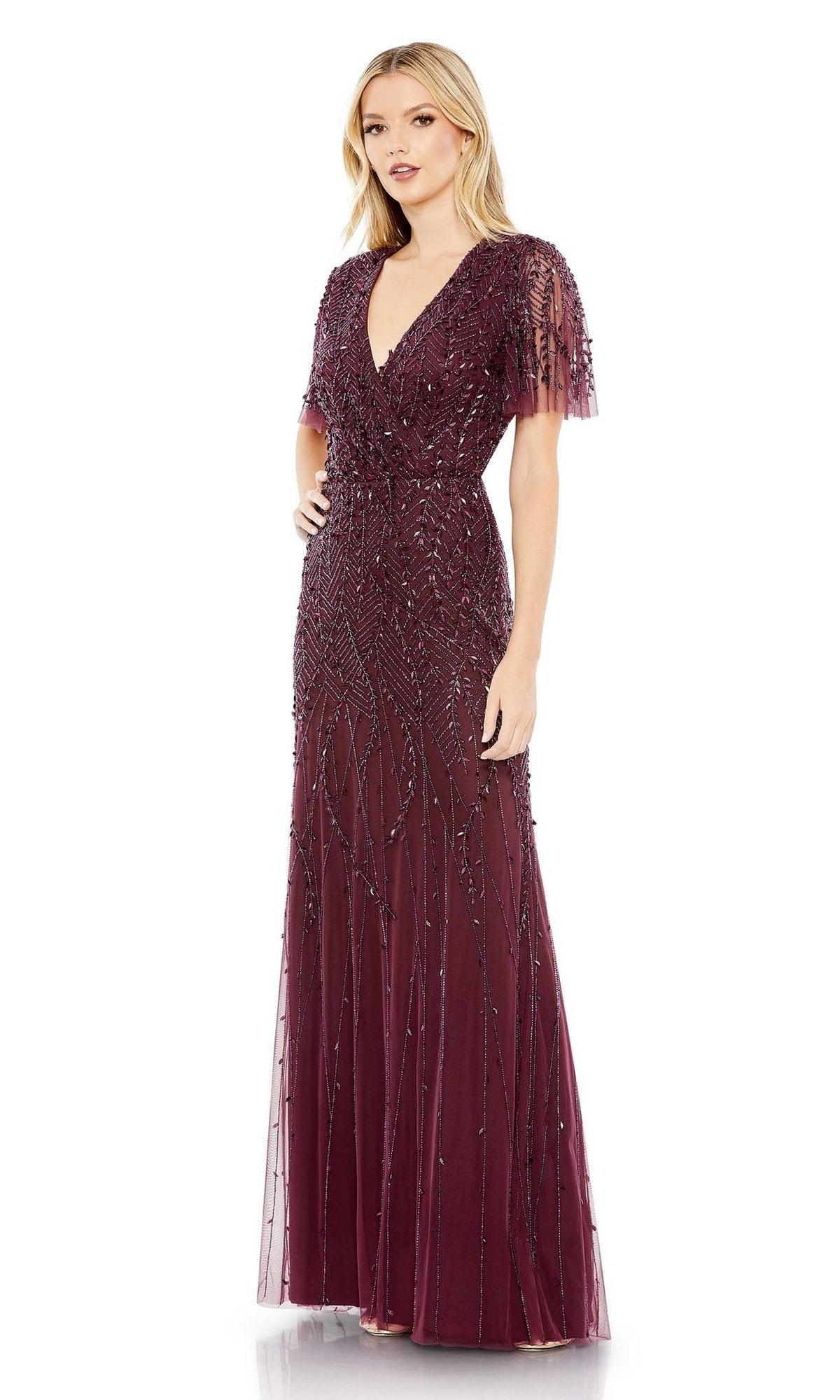 A woman wears the Mac Duggal 35109 Flutter-Sleeve Long Formal Dress in deep burgundy, featuring short flutter sleeves and lavish beaded embellishments for a stunning, floor-length evening look.
