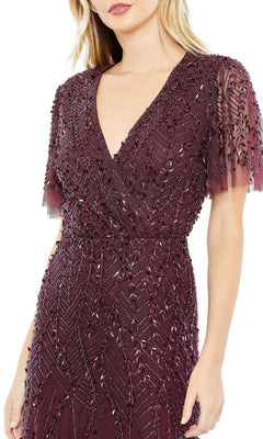 A woman wears the Mac Duggal 35109 Flutter-Sleeve Long Formal Dress in deep burgundy, featuring intricate bead and sequin leaf embellishments.