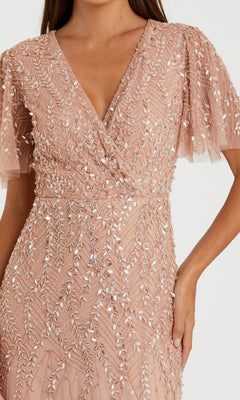 A woman wears the Mac Duggal 35109 Flutter-Sleeve Long Formal Dress in blush pink, featuring short flutter sleeves and detailed leaf-pattern bead and sequin embellishments.
