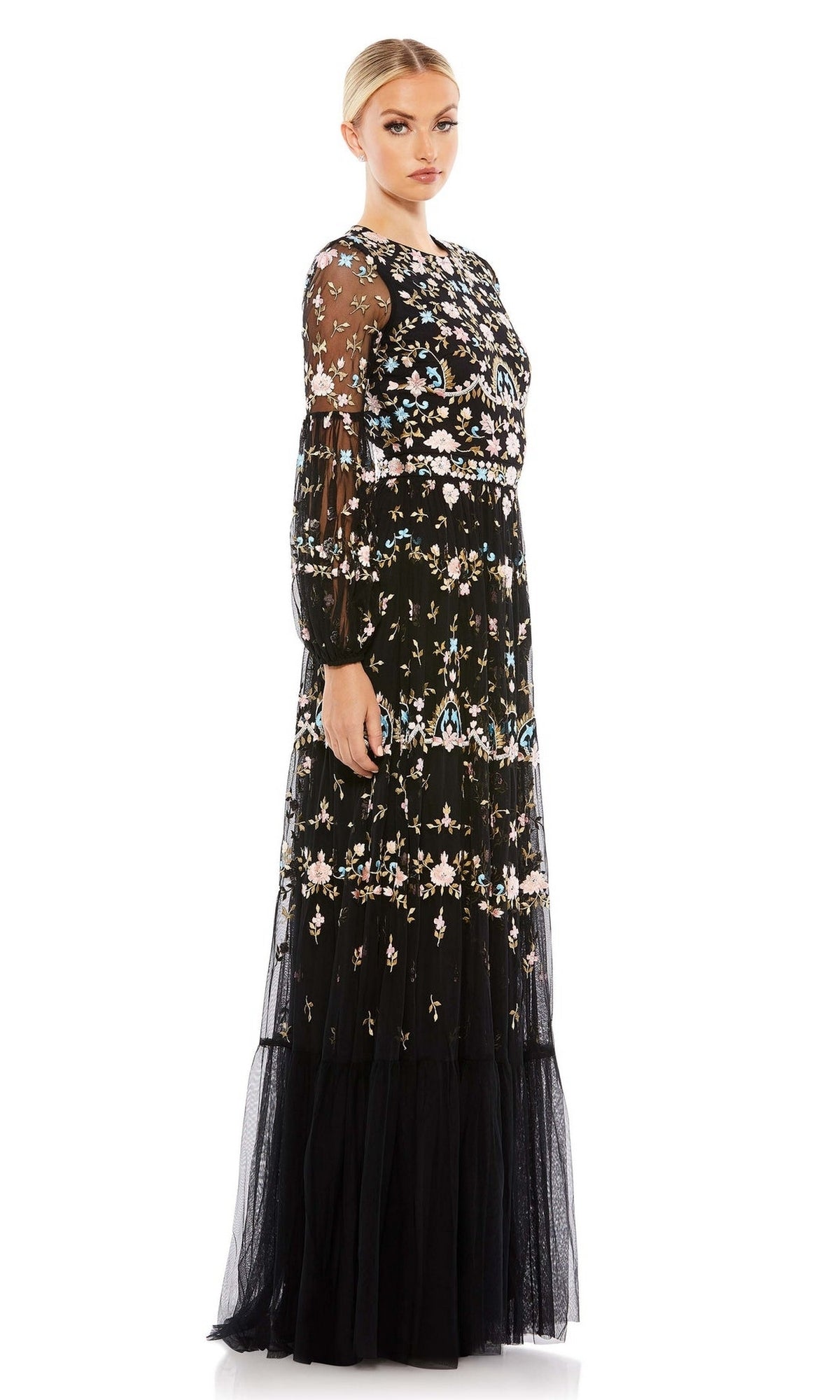 A woman stands against a white background wearing the Long Formal Dress 35111 by Mac Duggal, featuring floral embroidery, long black sheer gown, long sleeves, and a fitted waist.