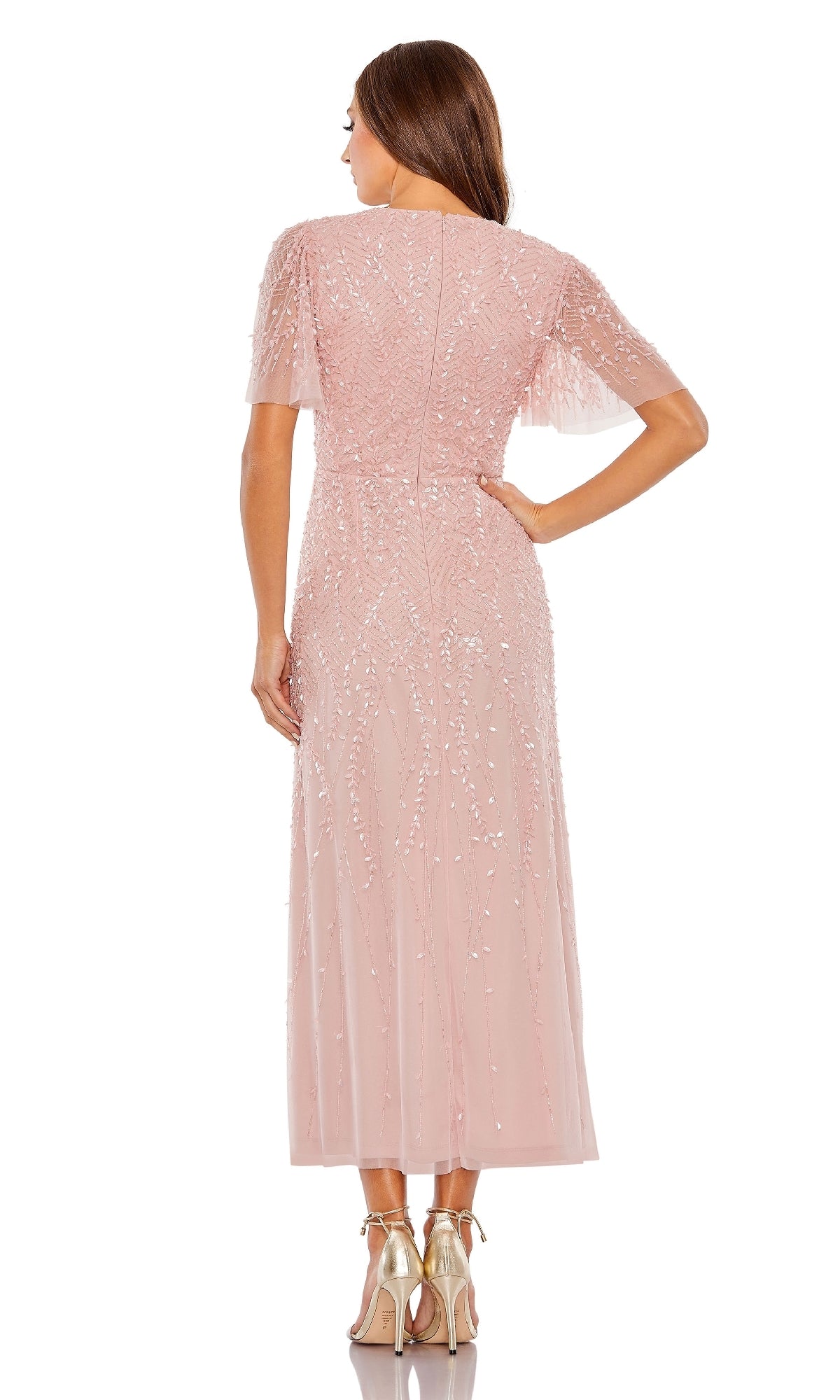 A woman faces away wearing the Mac Duggal 35116 Beaded Midi Semi-Formal Dress in blush pink with short sleeves, sequin embellishments, and gold high heels against a white background.