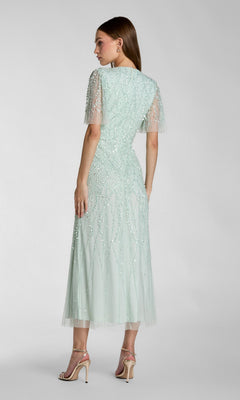 A woman wears the Mac Duggal 35116 Beaded Midi Semi-Formal Dress in light mint green with short sleeves and nude heels, posing against a plain background—a stylish option for any semi-formal occasion.