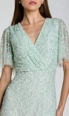 A woman wearing the Mac Duggal 35116 Beaded Midi Semi-Formal Dress in light green, featuring short sleeves, sequin and bead details, and a flattering V-neckline—ideal for any semi-formal event.
