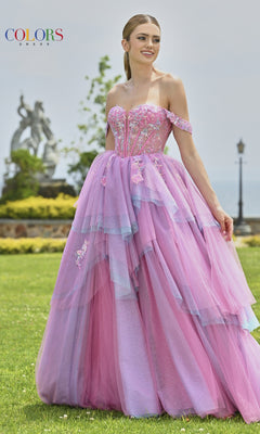 A woman stands on grass framed by trees and a statue, wearing the Off-Shoulder Long Prom Ball Gown: Colors Dress 3534, a multi-colored formal dress with layered lavender and pink hues.